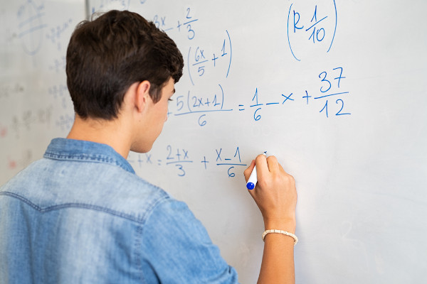 Garoto fazendo cálculos matemáticos em um quadro branco.
