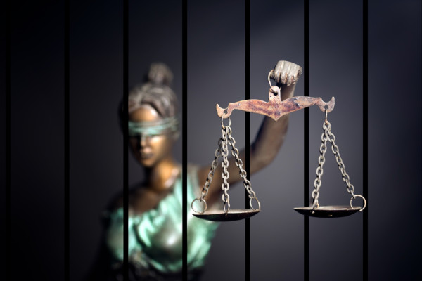 Estátua símbolo da justiça atrás das grades em referência à pena por feminicídio.